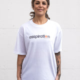Woman standing facing forwards with arms at her sides, wearing a white unisex oversized t-shirt with a boxy fit made from premium poly-cotton jersey, featuring the A$$piration Project logo on the front in grey, peach and green.