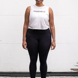Woman standing facing forward with her arms by her sides, wearing a cropped bamboo-organic cotton tank in cream, featuring the A$$piration Project logo on the front in grey, peach and green.