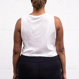 Woman standing facing backwards with her arms by her sides, wearing a cropped bamboo-organic cotton tank in cream.