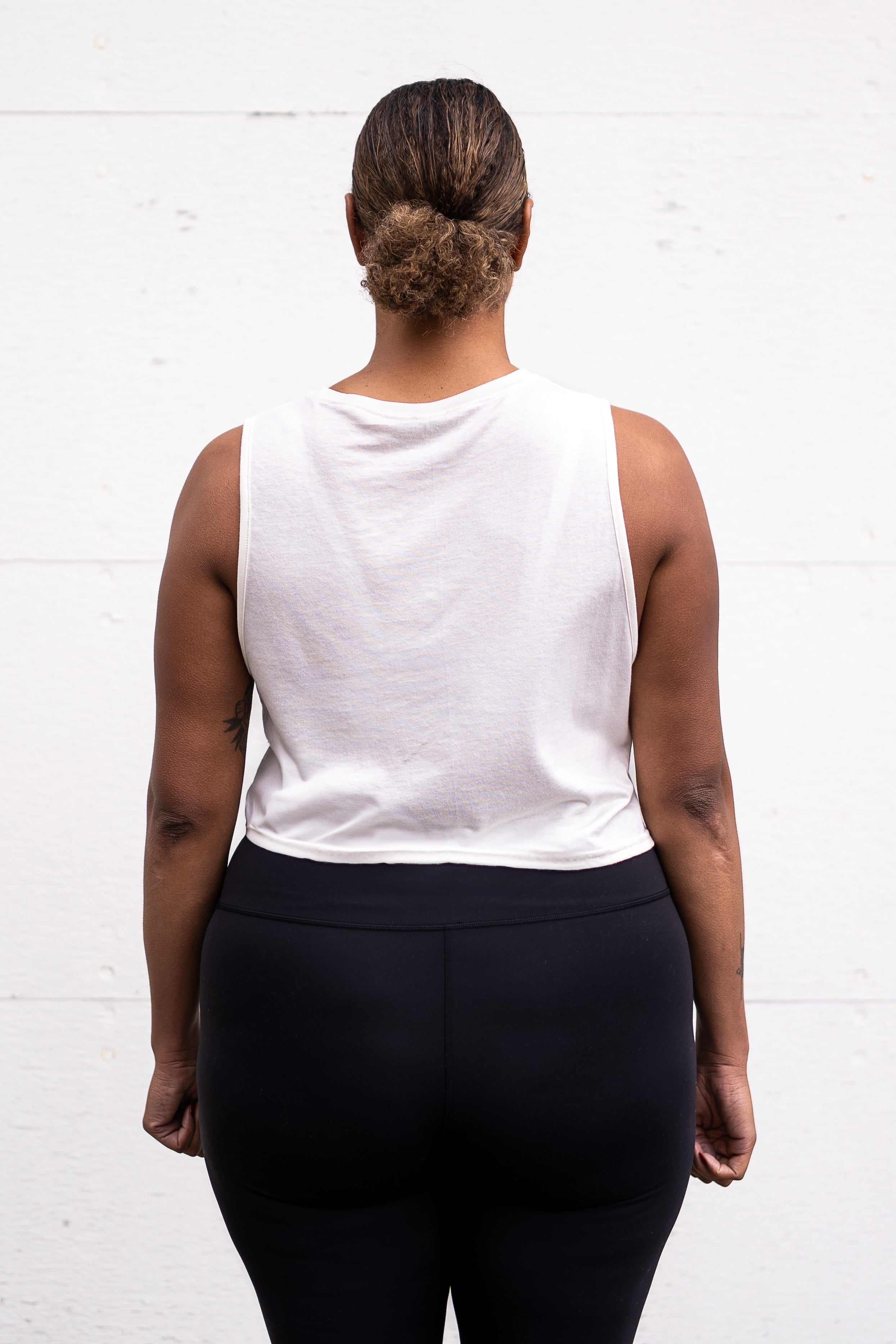 Woman standing facing backwards with her arms by her sides, wearing a cropped bamboo-organic cotton tank in cream.