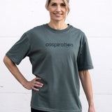 Woman standing facing forward with one hand on hip, wearing a sage green unisex oversized t-shirt with a boxy fit, made from premium poly-cotton jersey, featuring the A$$piration Project logo on the front in a tone on tone darker sage green.