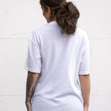 Woman standing facing backwards wearing a white unisex oversized t-shirt with a boxy fit made from premium poly-cotton jersey.