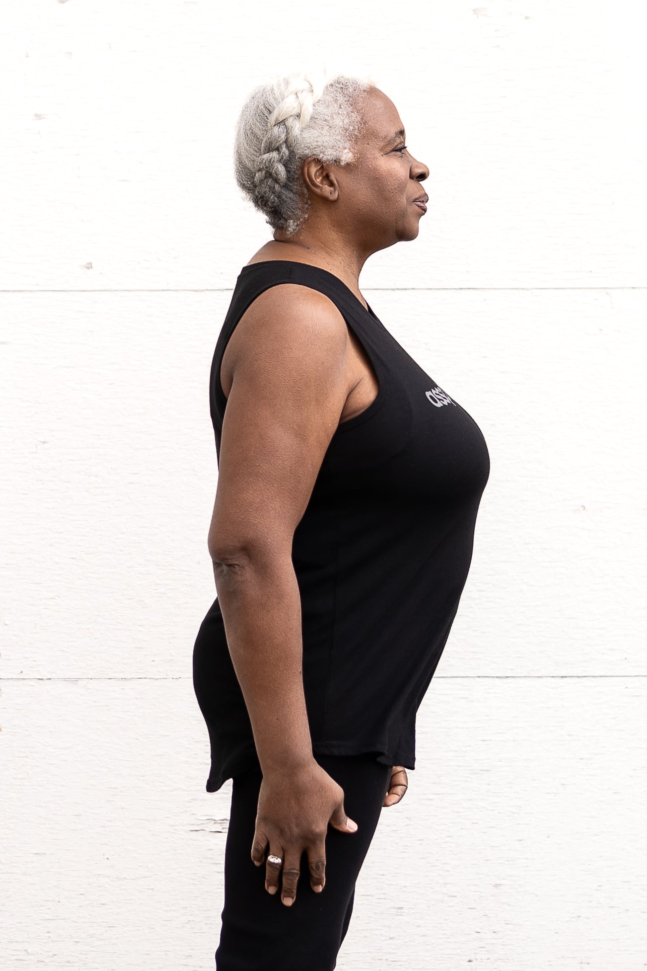 Woman standing facing sideways wearing a full-length bamboo-organic cotton tank in black, featuring a relaxed fit and rounded hem, featuring the A$$piration Project logo on the front in light grey.