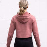 Woman standing facing backwards wearing a cropped bamboo-organic cotton fleece hoodie in dusty rose, featuring a finished hem.