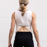 Woman standing facing backwards wearing a full-length bamboo-organic cotton tank in cream, displaying the back hem tucked into her sports bra.