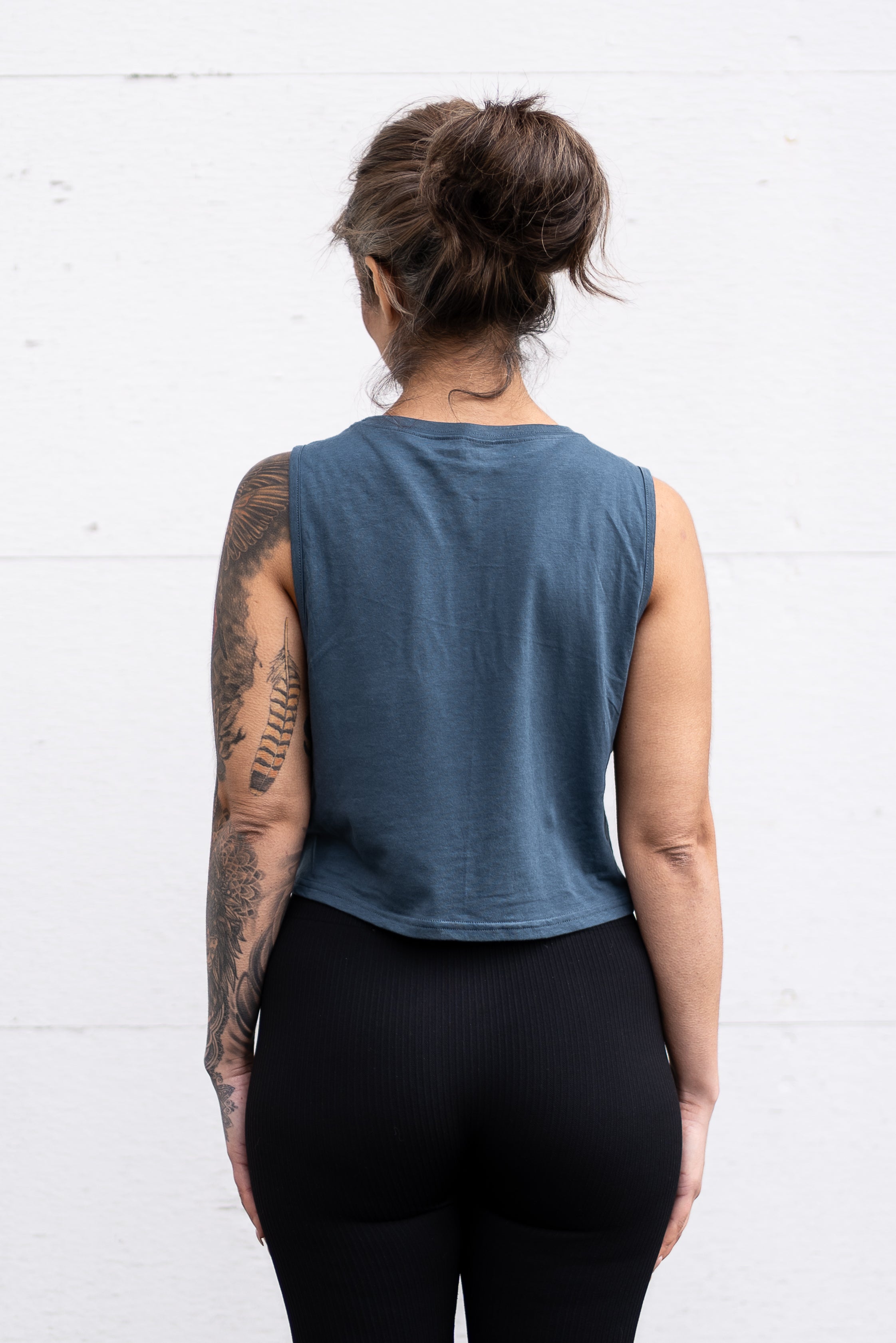 Woman standing facing backwards with her arms by her sides, wearing a cropped bamboo-organic cotton tank in slate blue.