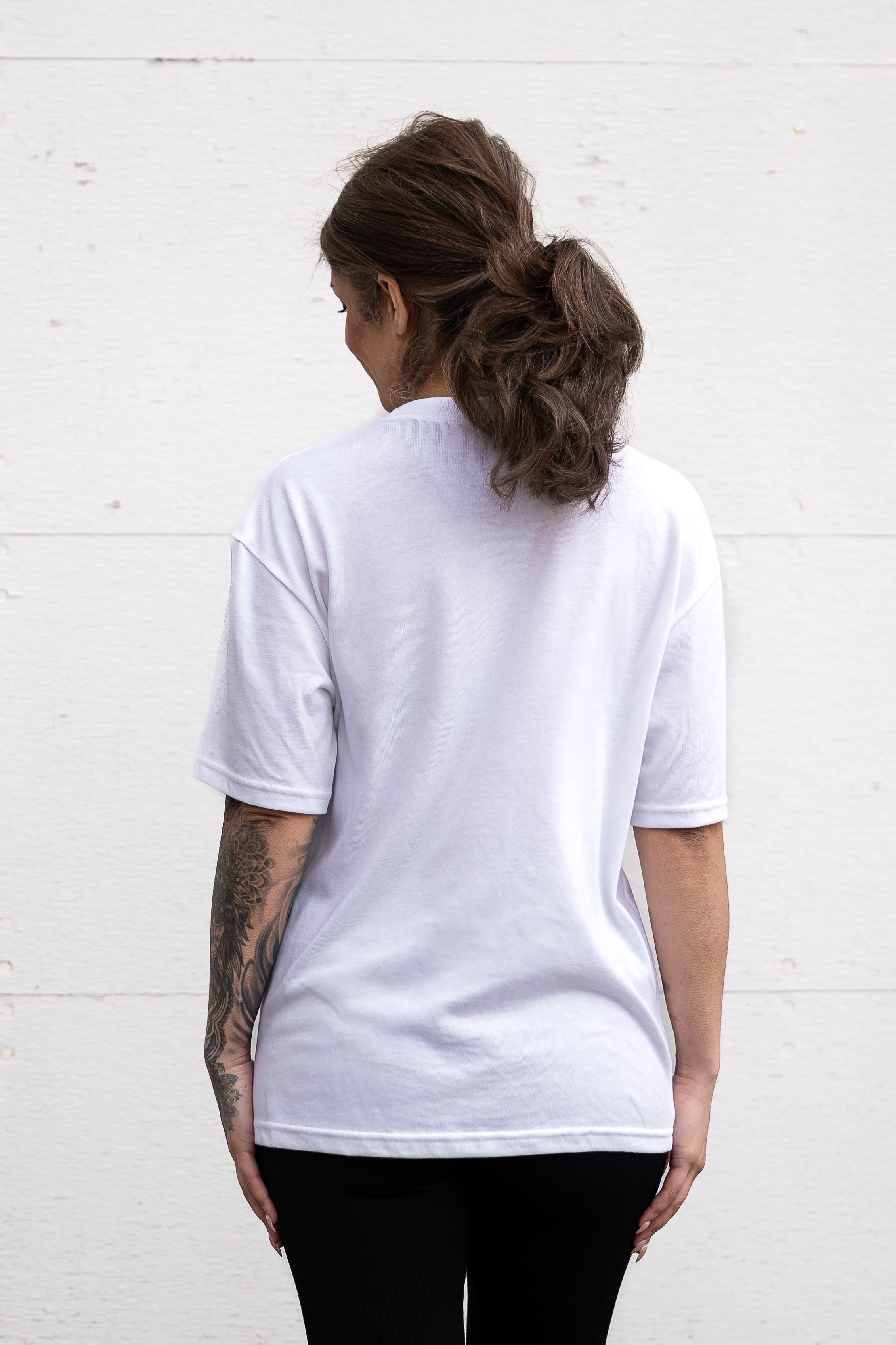 Woman standing facing backwards wearing a white unisex oversized t-shirt with a boxy fit  made from premium poly-cotton jersey.