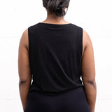 Woman standing facing backwards with her arms by her sides, wearing a cropped bamboo-organic cotton tank in black.