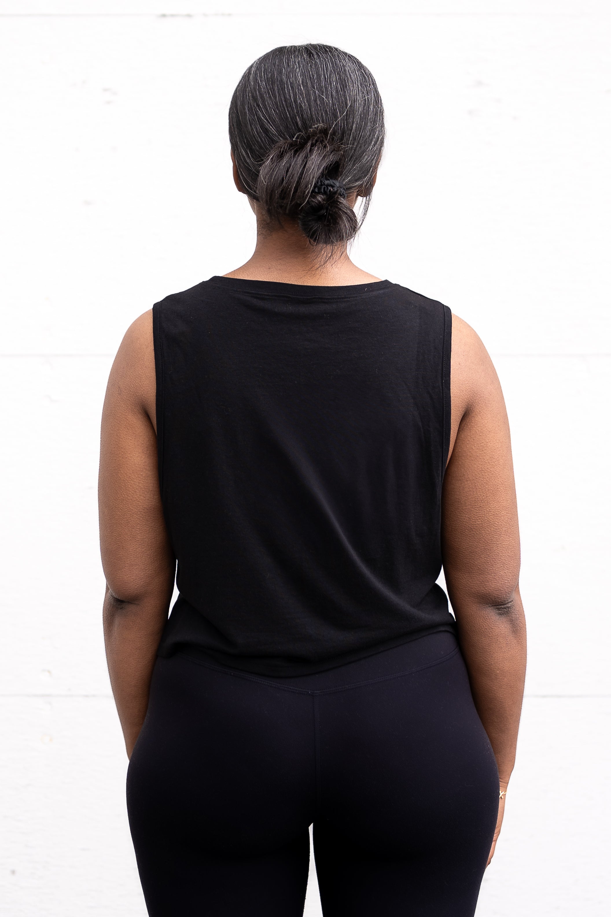 Woman standing facing backwards with her arms by her sides, wearing a cropped bamboo-organic cotton tank in black.