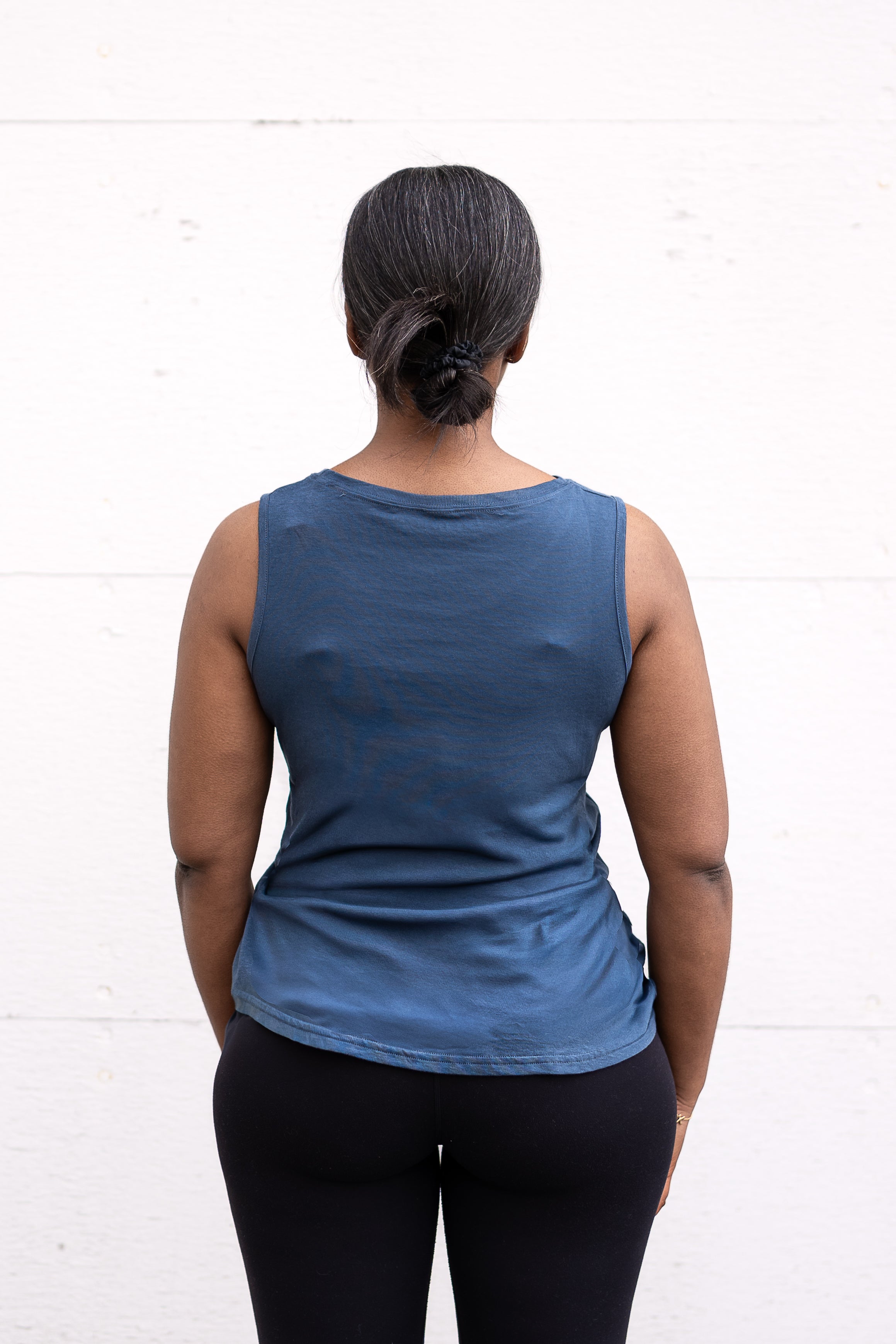 Woman standing facing backwards, wearing a full-length bamboo-organic cotton tank in slate blue, featuring a relaxed fit and rounded hem.