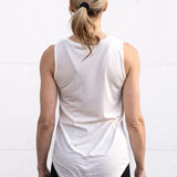Woman standing facing backwards wearing a full-length bamboo-organic cotton tank in cream, featuring a relaxed fit and rounded hem.
