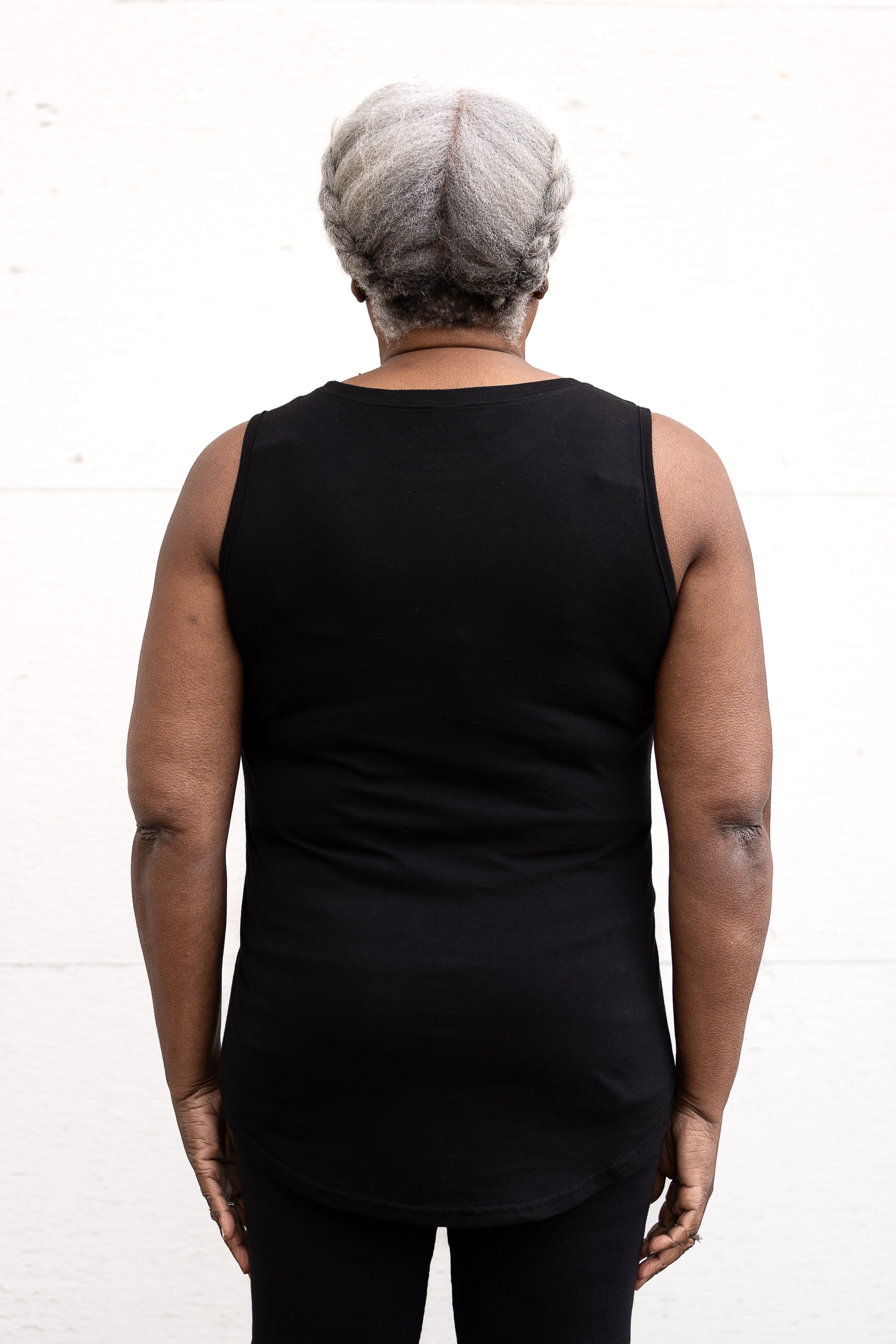 Woman standing facing backwards, wearing a full-length bamboo-organic cotton tank in black, featuring a relaxed fit and rounded hem.