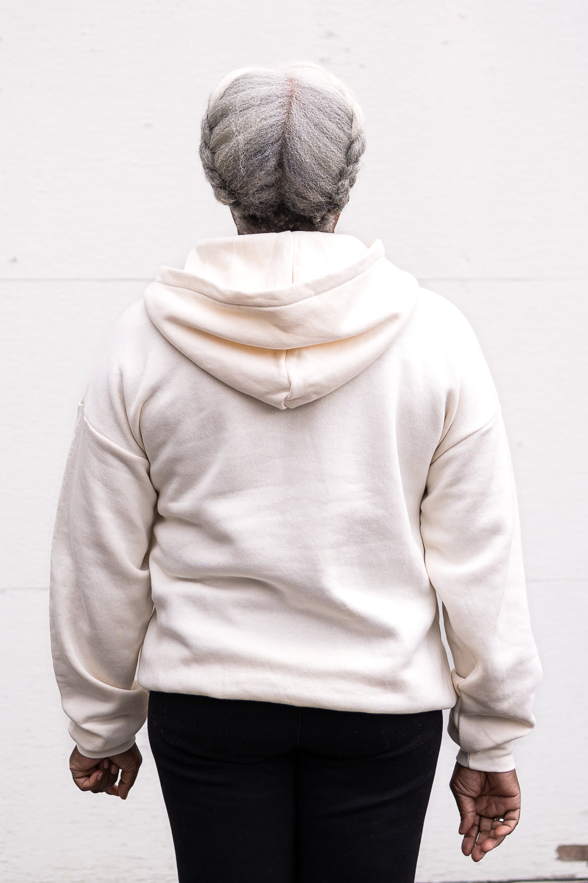 Woman standing facing forward with arms at her sides, wearing a unisex oversize bamboo-organic cotton fleece hoodie in cream, with dropped shoulders and a large kangaroo pocket.