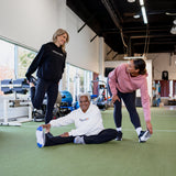 Three women stretching in a gym, wearing unisex oversize bamboo-organic cotton fleece hoodies in black, cream and dusty rose with dropped shoulders and a large kangaroo pocket, featuring the A$$piration Project logo on the front.